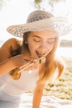 一名戴帽子的妇女在阳光明媚的公园里用筷子享用寿司野餐