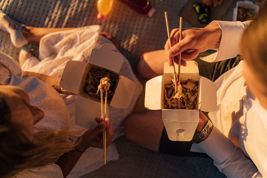 两人在轻松的野餐中享用外卖面条，营造出舒适的户外氛围