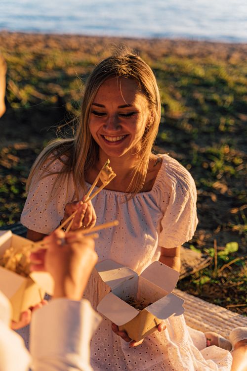 Free Woman smiling during a sunset picnic with takeout food by the water. Stock Photo