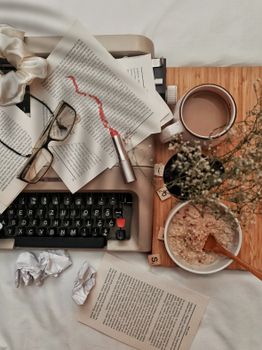 A cozy workspace featuring a vintage typewriter, oatmeal bowl, coffee, eyeglasses, and dried flowers.
