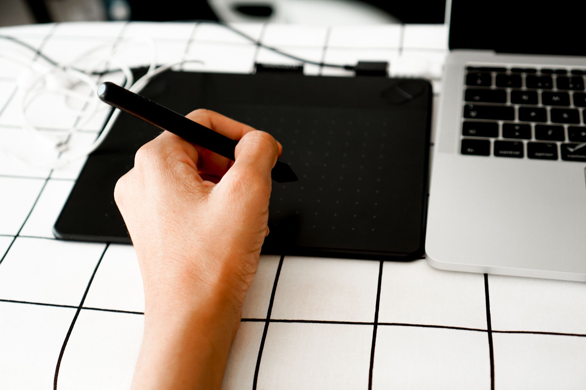 Close-up of a hand using a pen tablet next to a laptop, ideal for digital design projects.