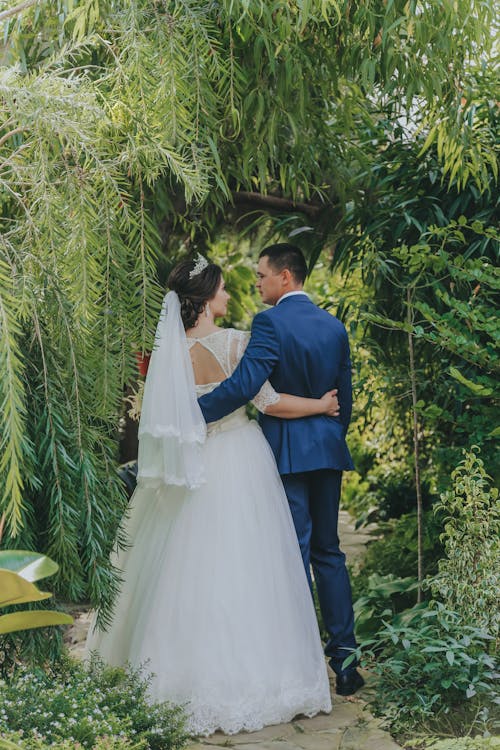 Free Full body of young couple in wedding clothes hugging and looking at each other in green garden Stock Photo