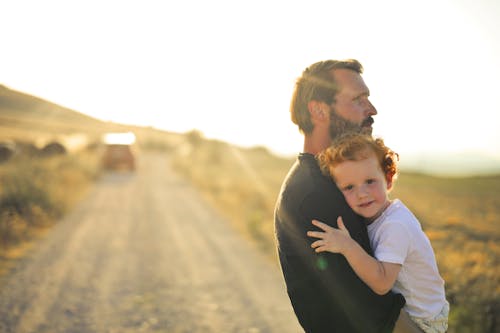 Free Man in Black Shirt Standing on the Road Carrying a Boy Stock Photo