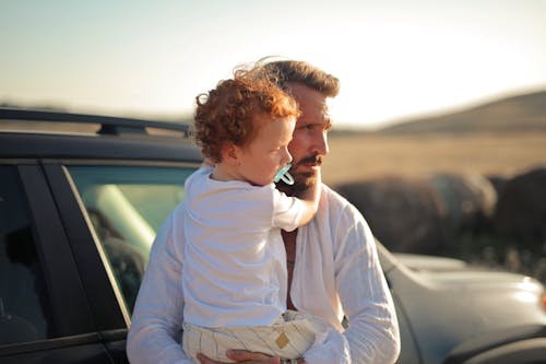 Man Standing next to a Car Holding a Child