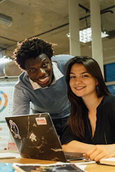 在现代化的办公室里，两位不同的同事面带微笑地一起工作