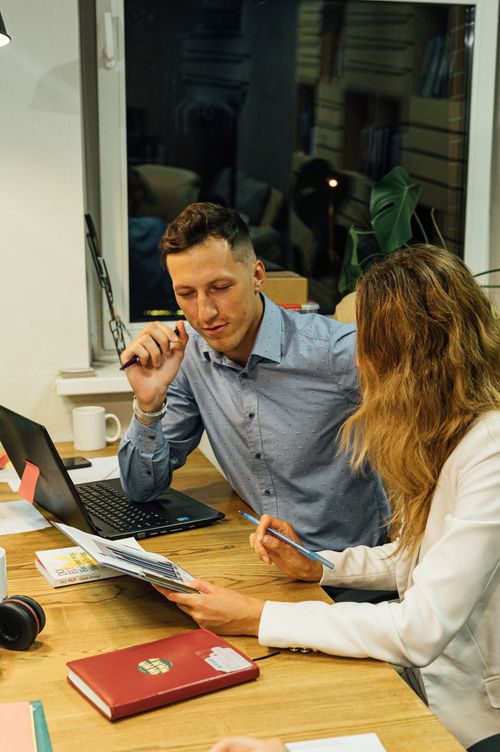 Free Two adults collaborate on reports at an office desk, engaging in a focused discussion. Stock Photo