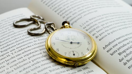 Close-Up Shot of a Gold Pocket Watch on a Book