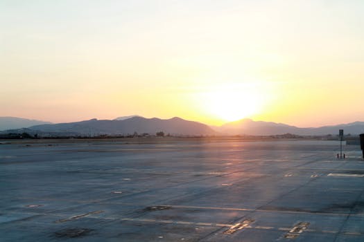 Tranquil view of an airport runway with the sun rising over distant mountains, casting a gentle glow.
