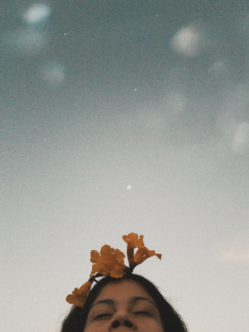 Peaceful close-up of a woman with yellow flowers under a clear sky.