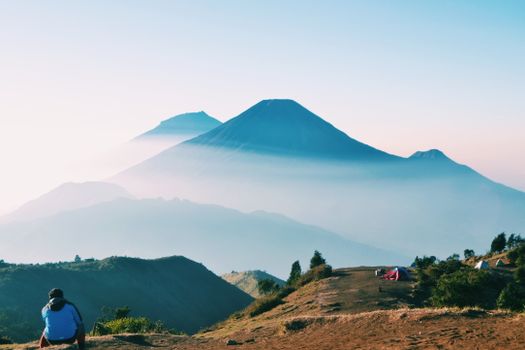 A serene sunrise over Central Java mountains with a camper in the foreground.