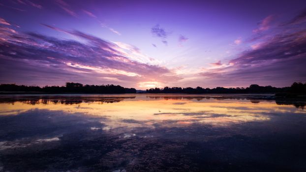 Serene landscape of a tranquil sunset reflecting on calm ocean waters, highlighting vibrant purple and orange skies.