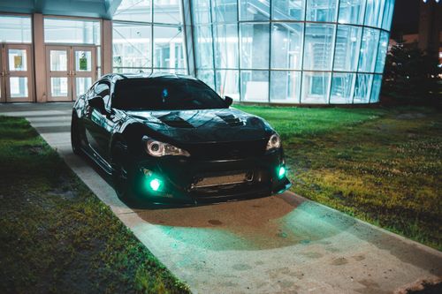 Free Contemporary sparkling automobile parked near green fresh lawn of glass building at night Stock Photo