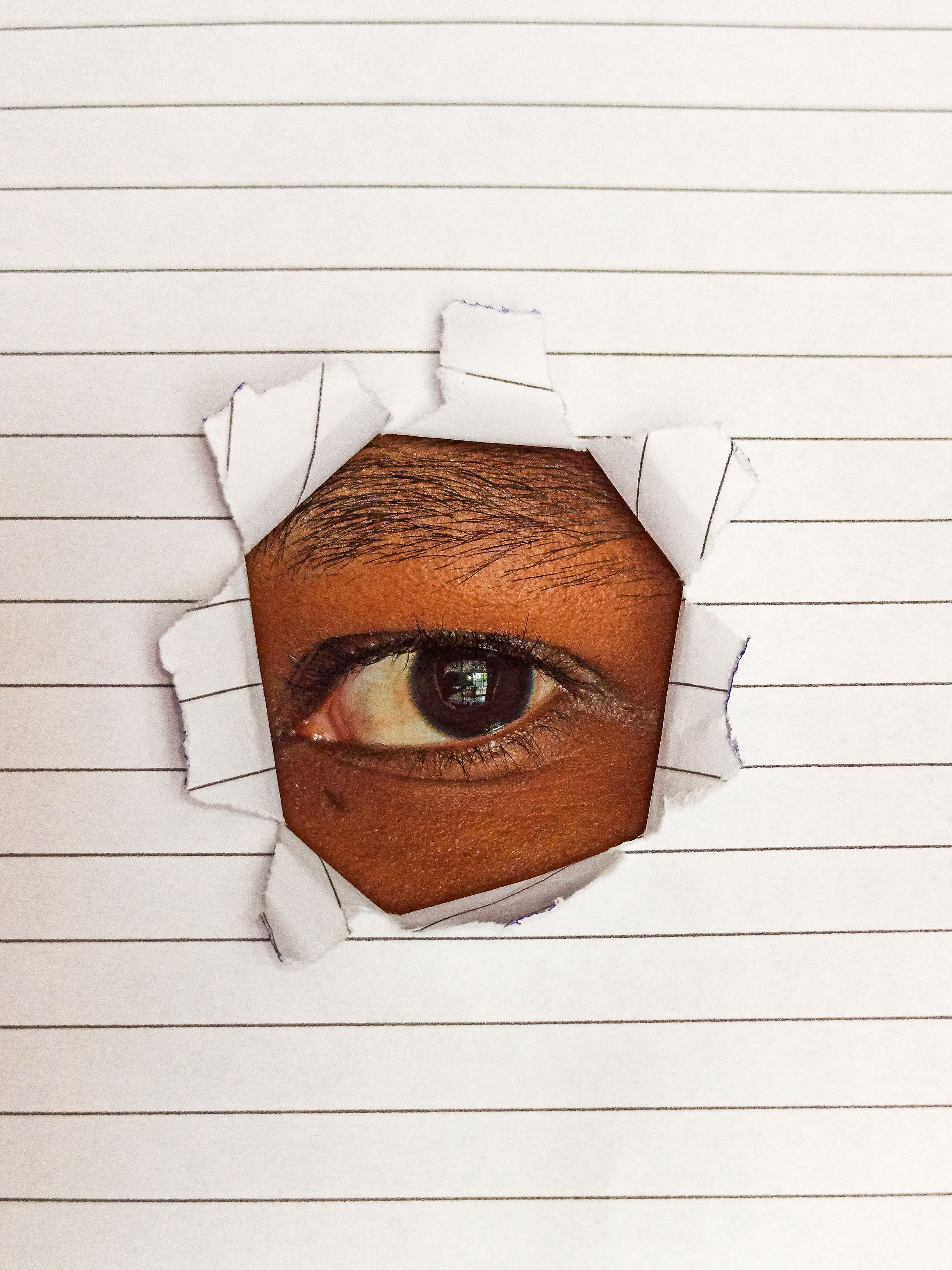 Close-up of a human eye peering through a hole in a lined paper, symbolizing curiosity.