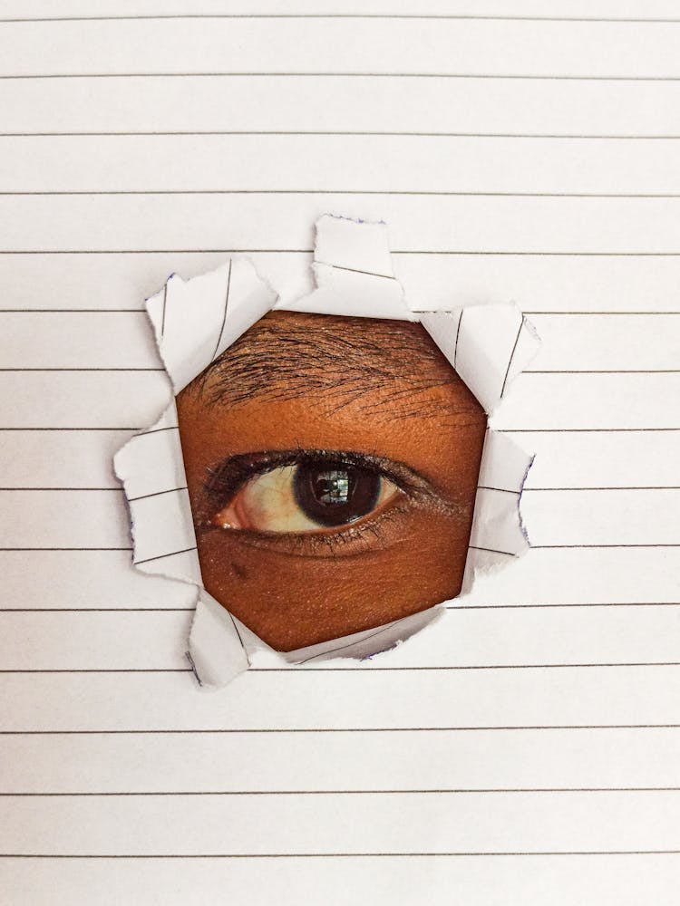 Close-up Of Eye Of A Person Looking Through A Hole In Paper 