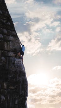 A man climbing a steep rocky mountain against a sunrise backdrop symbolizing determination and courage.