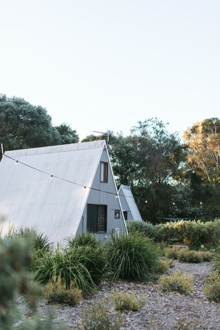Unusual triangular cottages placed on ground with lush green bushes in countryside against cloudless sky and tall trees in nature