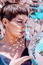 Charming female with bright glitter from silver disco ball looking into distance while standing on foil background