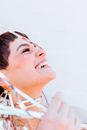 Crop positive female with closed eyes covered with decorative foil tinsel while standing on white background with head thrown back