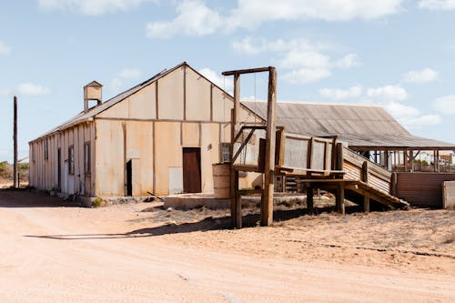 Aged countryside warehouse exteriors against empty roadway under blue cloudy sky on sunny day