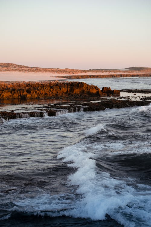 Spectacular view of foamy ocean with ripples and fast water flows against mount at sunset