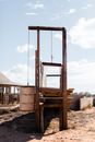 Aged wooden construction with reinforced concrete blocks hanging above sandy land under cloudy sky in sunlight