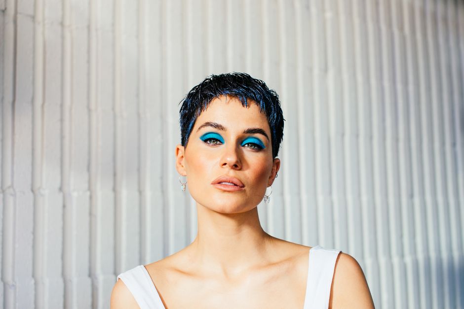 Young tender female with short hair and blue eyeshadow on eyelids looking at camera