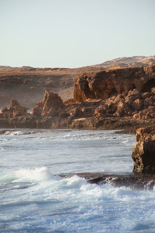 Spectacular view of mountain and rocky formations against wavy sea with fast water streams in storm