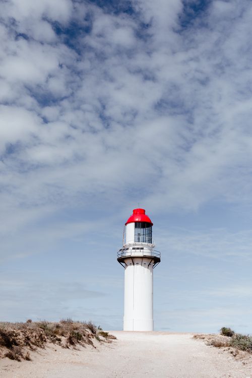 Free Scenic view of aged lighthouse on dry coast with grass under sky with fluffy clouds Stock Photo
