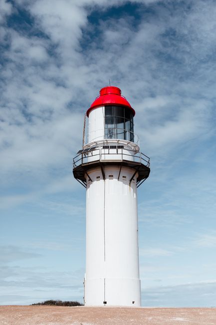 From below of aged beacon with fence on dry coast under cloudy sky in daylight