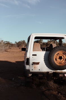 一辆报废的汽车停在干燥的沙质沙漠中，车身有明显的铁锈，还装着一个备用轮