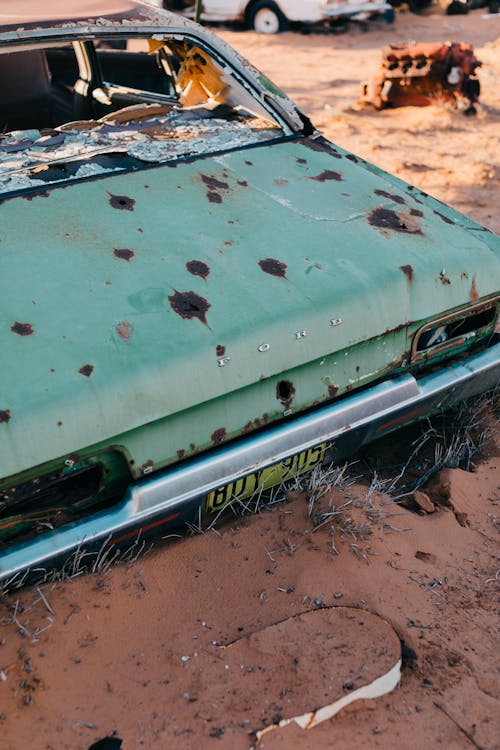 From above of old abandoned automobile with rusty bonnet placed on sandy ground in countryside in daytime