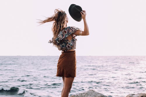 Stylish female standing against ocean in windy day