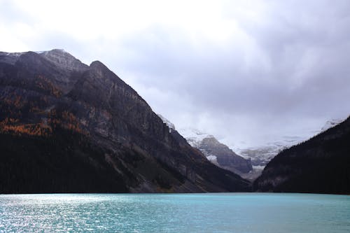 Picturesque landscape of blue water surface of pond surrounded by rocky mountainous terrain under cloudy sky