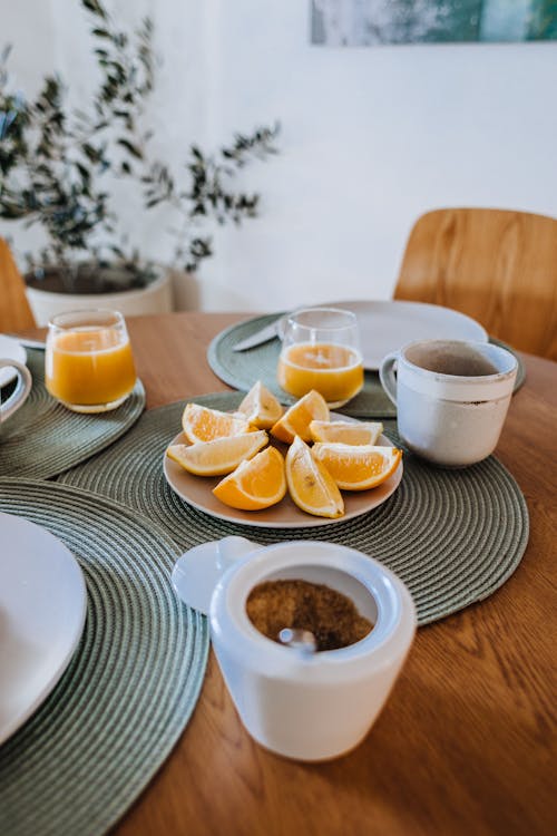 High angle of cut juicy oranges on ceramic plate near mug and juice on table in morning