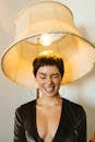 Positive female with short hair wearing decollete dress making funny face under floor lamp