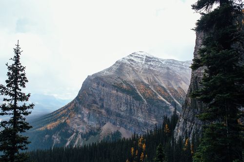 Free Picturesque scenery of rocky mountains with snowy peaks located among evergreen trees in highland Stock Photo