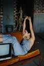 Side view of female with hands up sitting on wooden sofa with legs on vintage TV set in tailor workshop