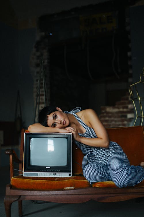 Free Peaceful female wearing overall lying on vintage TV set sitting on seethe in tailor workshop for sale Stock Photo