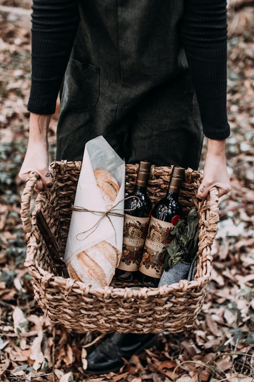 Person carrying basket with fresh bread and wine
