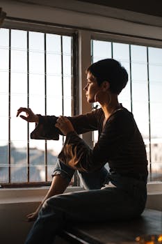 Young woman with short hair sitting by a window, lost in thought during a calm afternoon.