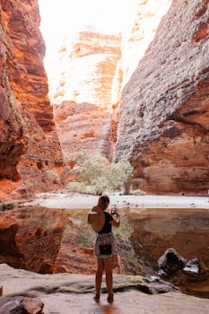 Woman photographing stunning canyon landscape with smartphone and hat.