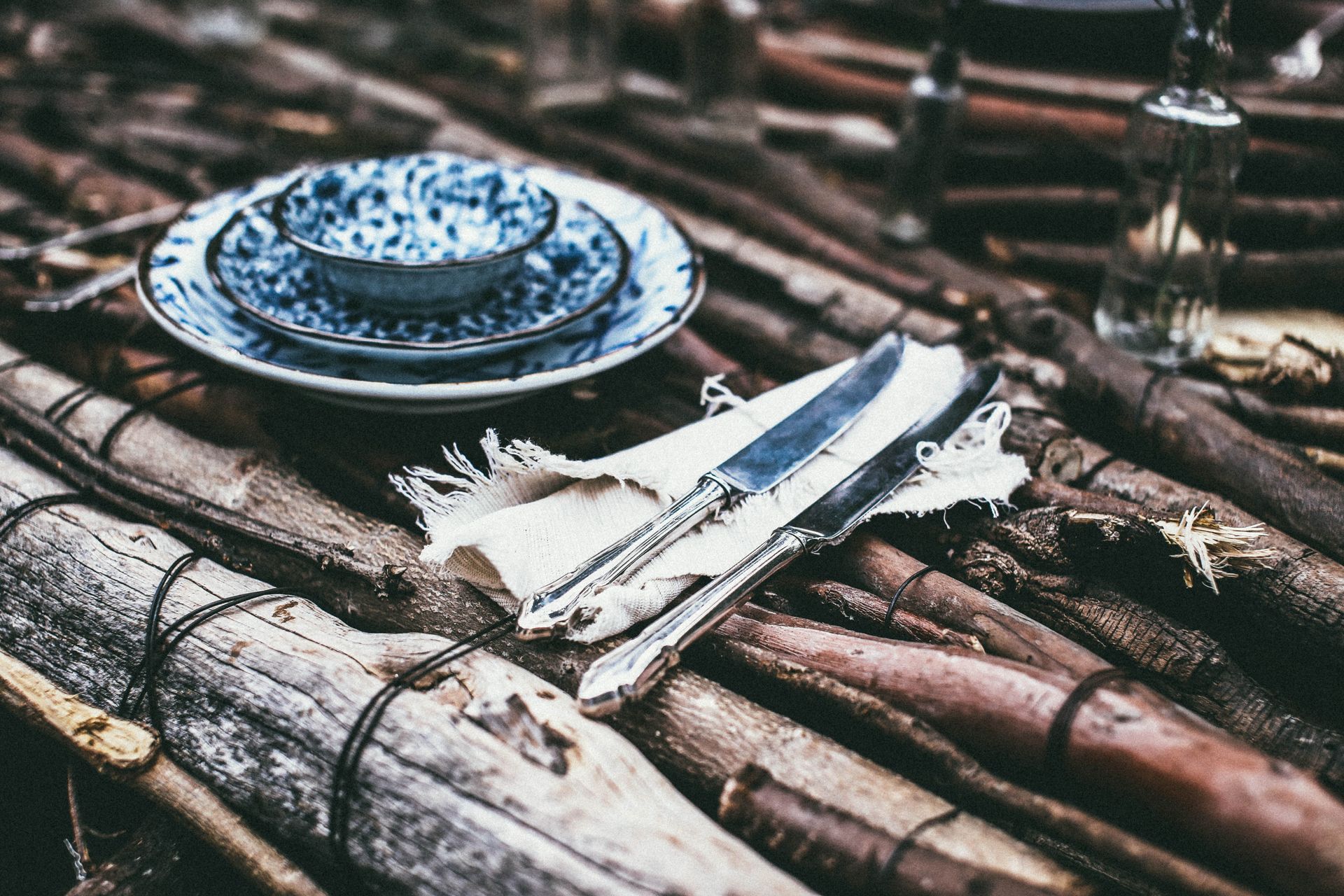 Table made of tree branches with plates and knifes near glass bottles in daytime