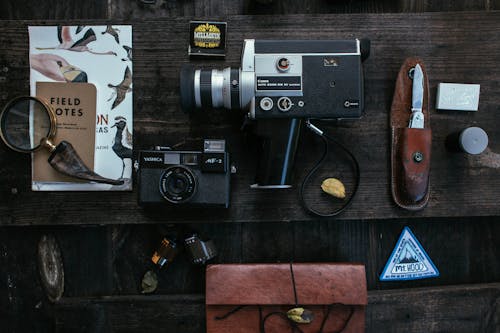 Overhead of vintage cameras near camera roll and knife near book about birds and lens placed on wooden table