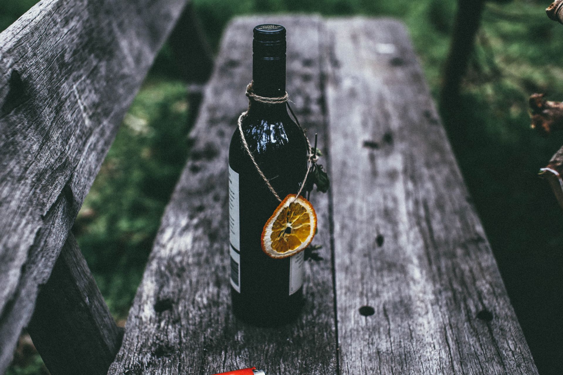 From above of glass bottle of wine with dried orange placed on old wooden bench in nature in daytime