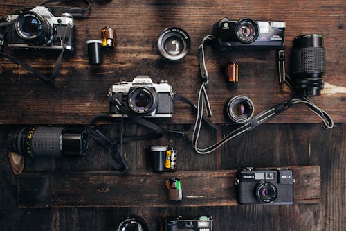Overhead of retro photo cameras near various lenses and films on wooden surface