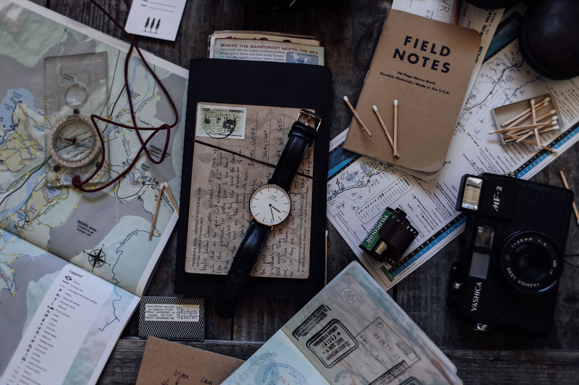 Travel kit laid out on a table with a paper map, watch, notebook and camera ready for a slower trip