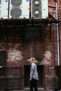 Side view of unrecognizable female with flying hair standing on street near aged house with air conditioning units in city