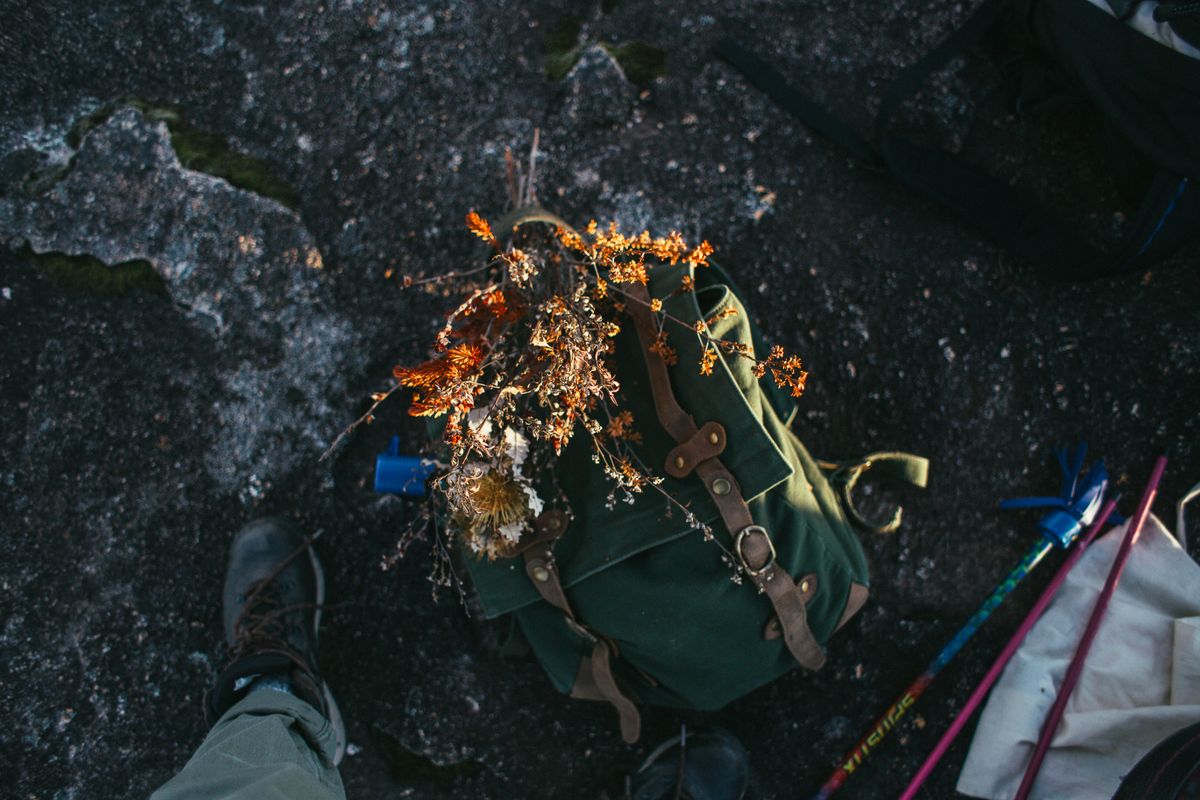 Rucsac verde asezat pe stanca, cu bete de trekking alaturi