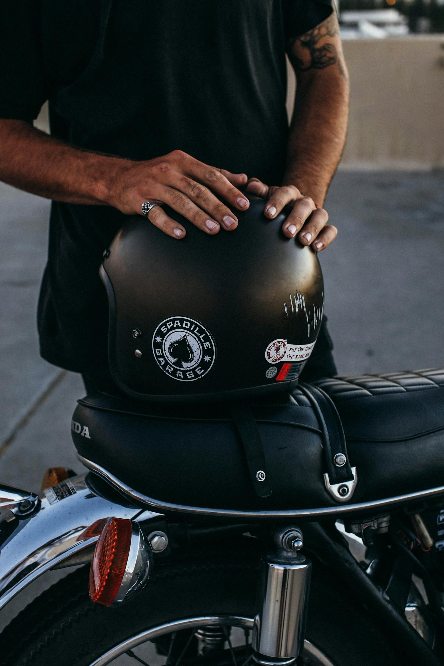 Unrecognizable tattooed ethnic male standing near modern motorcycle with hands on black helmet on sidewalk in street against concrete fence