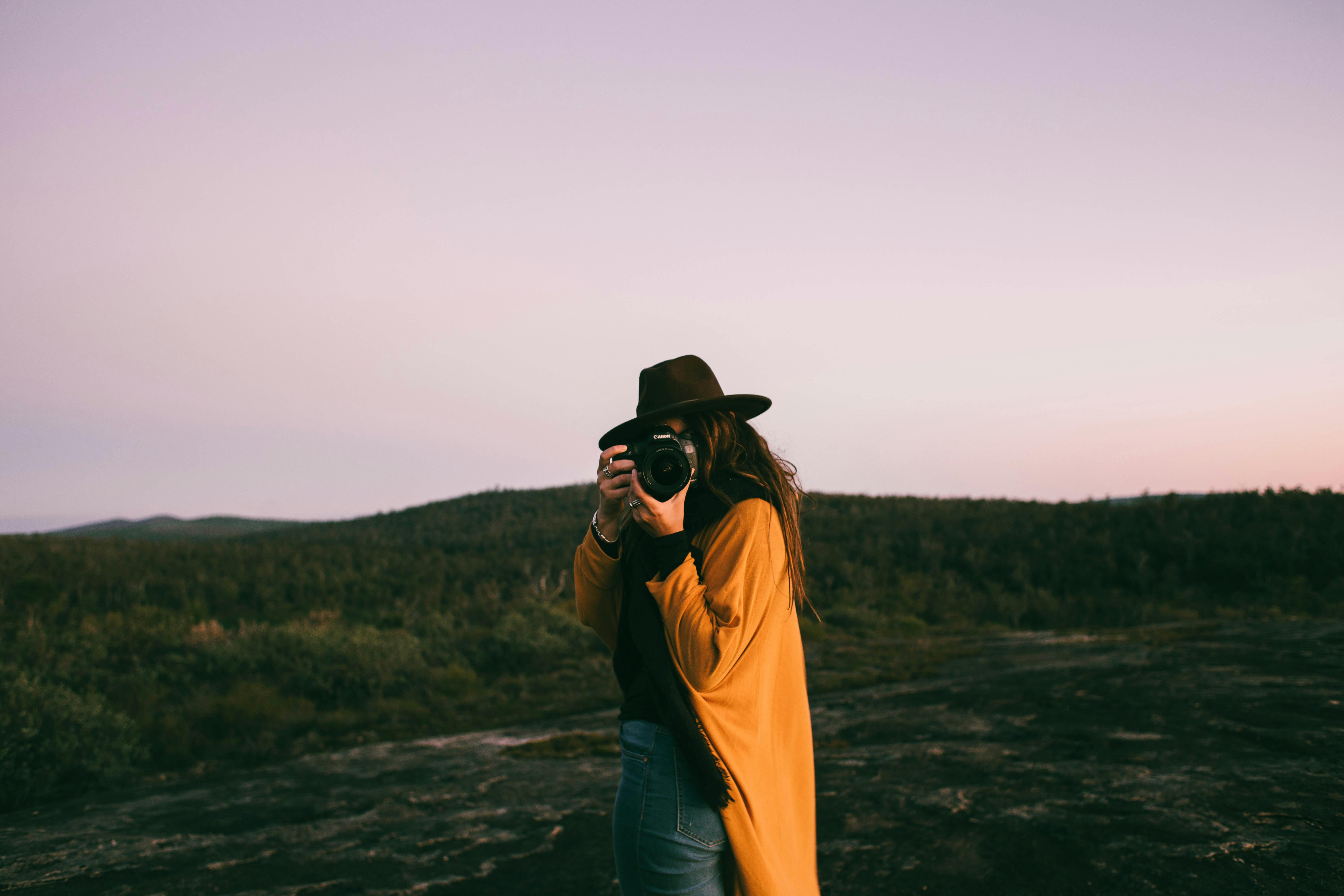 unrecognizable woman in hat taking photo in nature
